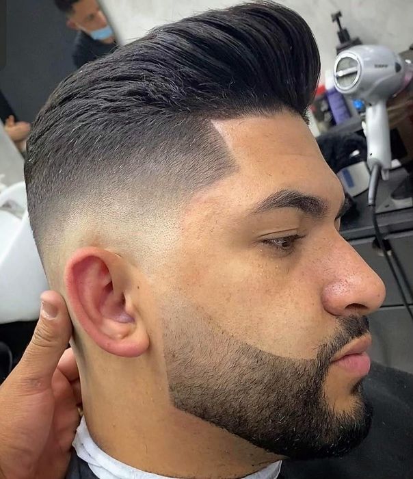 Skin fade con el pelo peinado hacia atrás y barba delineada